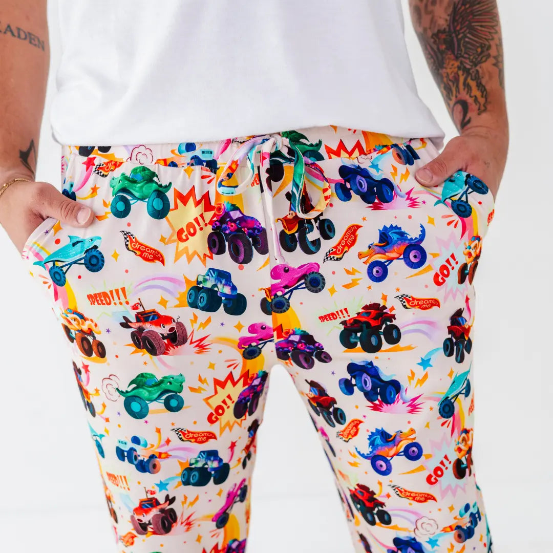 Close-up of men's pajama pants with a drawstring waist and a colorful monster truck print, hands in the pockets.